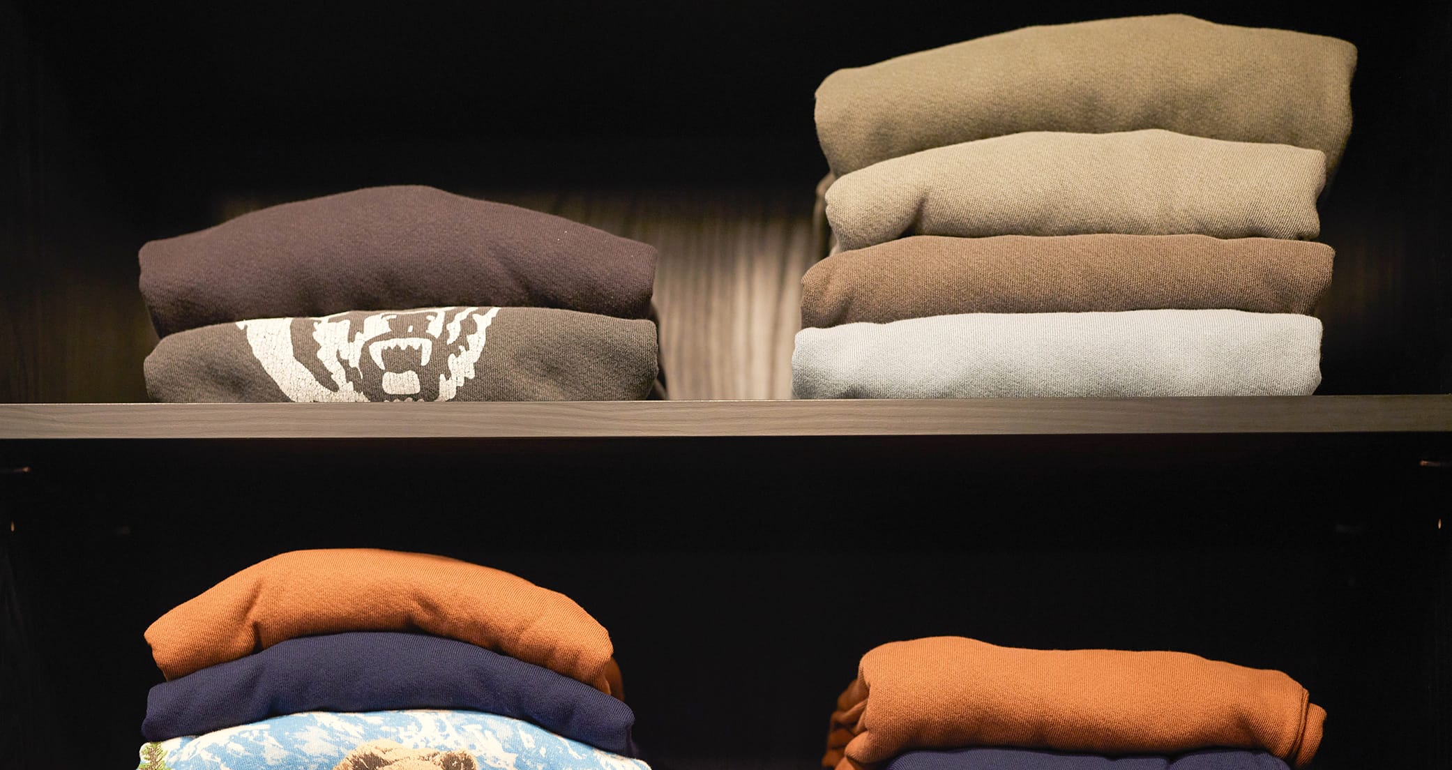 John Rankin’s custom shelving in a walk in closet in dark wood grain finish, holds folded sweaters by California Closets