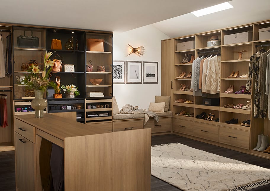 Walk in closet configured with center island for jewelry, with shoe wall, custom drawers and bench by California Closets