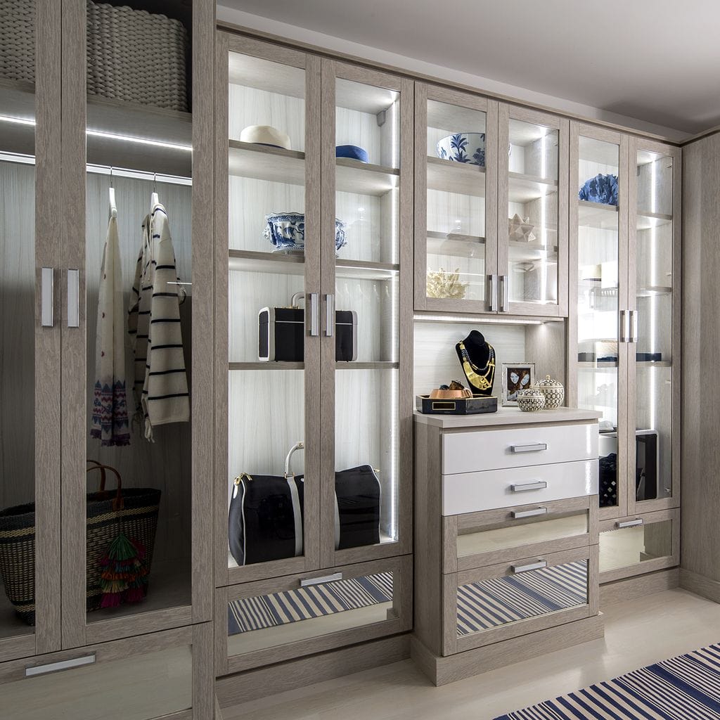 Closet designed with wardrobe cabinet glass doors and lighting by California Closets